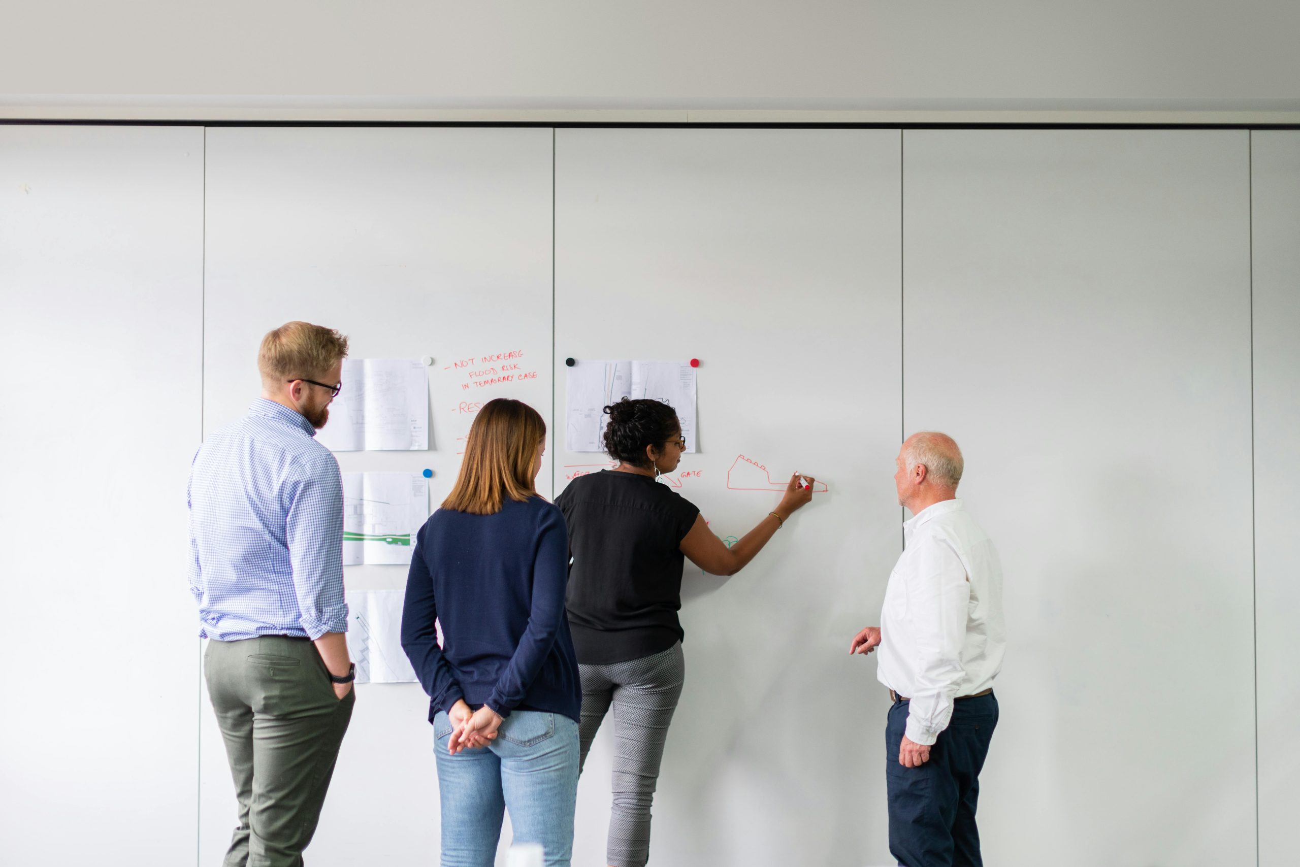 Photo shows four people writing on wall mounted paper, they are all facing the wall.